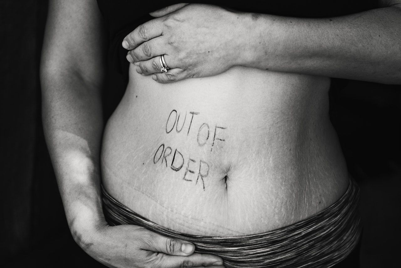 Persona sosteniendo su vientre inflamado y pone "out of order"